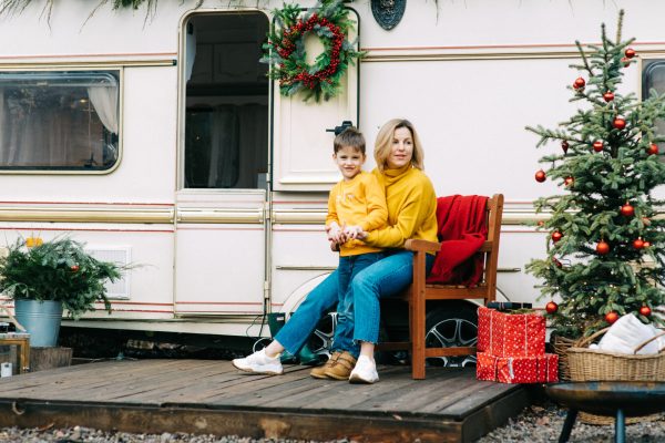 Beautiful mother and child boy with red cups drink cocoa or tea in trailer. Family vacation RV holiday trip, happy smiling family travel on camper, people in motorhome interior. Caravan in park